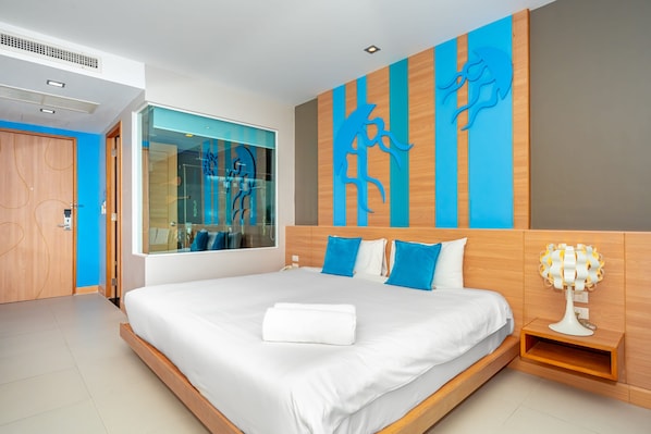 A modern hotel room with a large bed, a nightstand with a lamp, a mirror, and a view of the city. - Ratana Platinum Resort Kamala (Kamala)