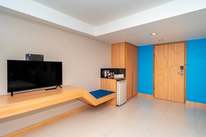 Una habitación moderna con televisión sobre un mueble de madera, una kitchenette pequeña y una puerta azul.