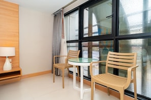 A room with a glass table, two wooden chairs, a white lamp, and a large window with a view. - Ratana Platinum Resort Kamala (Kamala)