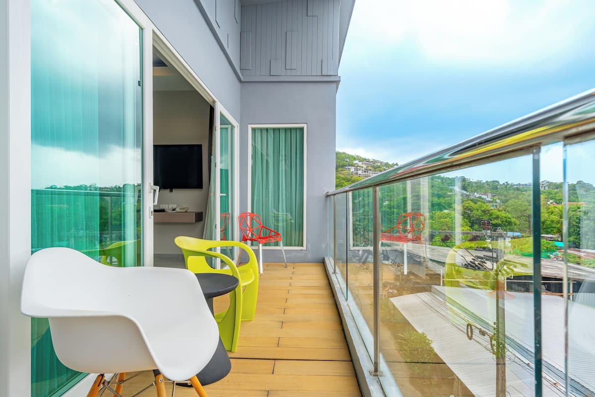 Een balkon met een houten vloer, een witte stoel, een gele stoel en een rode stoel.