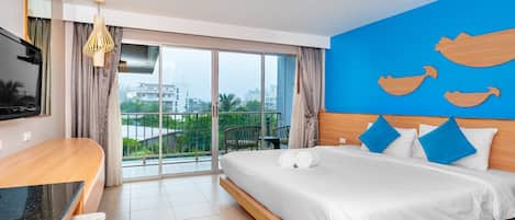 A hotel room with a bed, a TV, a balcony with a view, and a blue wall with wooden cutouts.