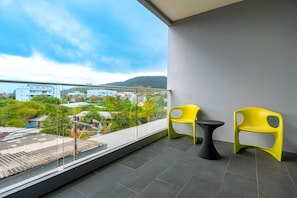 A balcony with two yellow chairs and a small table, overlooking a residential area with houses and greenery. - Ratana Platinum Resort Kamala (Kamala)