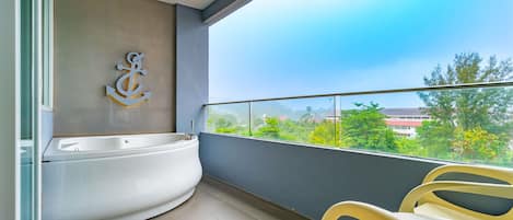 A balcony with a bathtub, chairs, and a view of greenery and buildings.