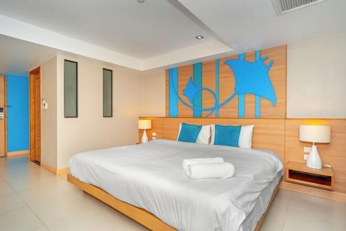 Une chambre d’hôtel avec un grand lit, deux lampes de chevet, une tête de lit en bois et une œuvre d’art abstraite bleue accrochée au mur.