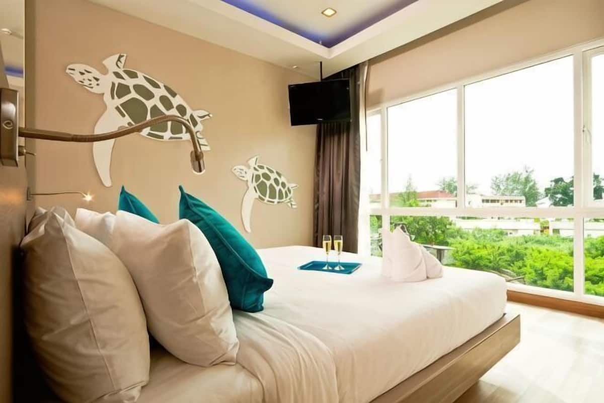 Een slaapkamer met een bed, kussens, een flatscreen televisie en een groot raam met uitzicht.
