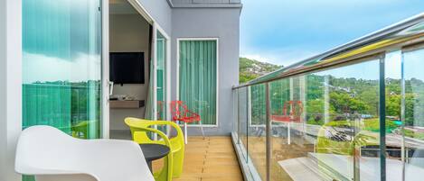 A balcony with a wooden floor, a white chair, a yellow chair, and a red chair.