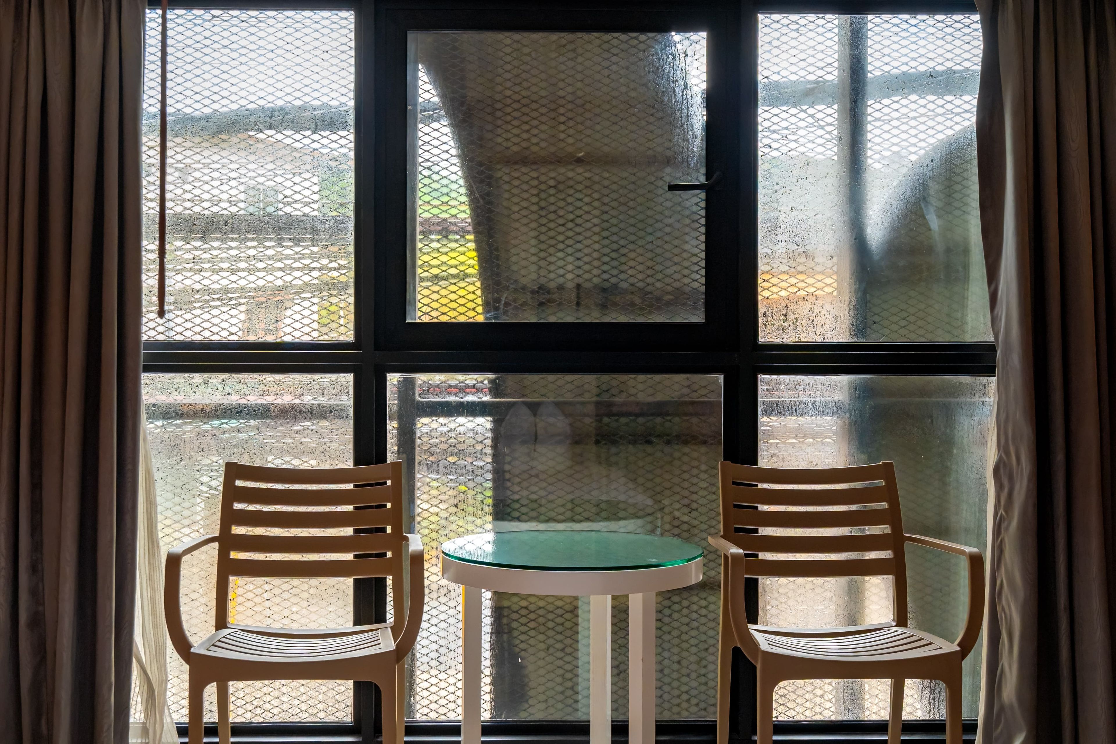 A room with a window, two wooden chairs, and a small round table.