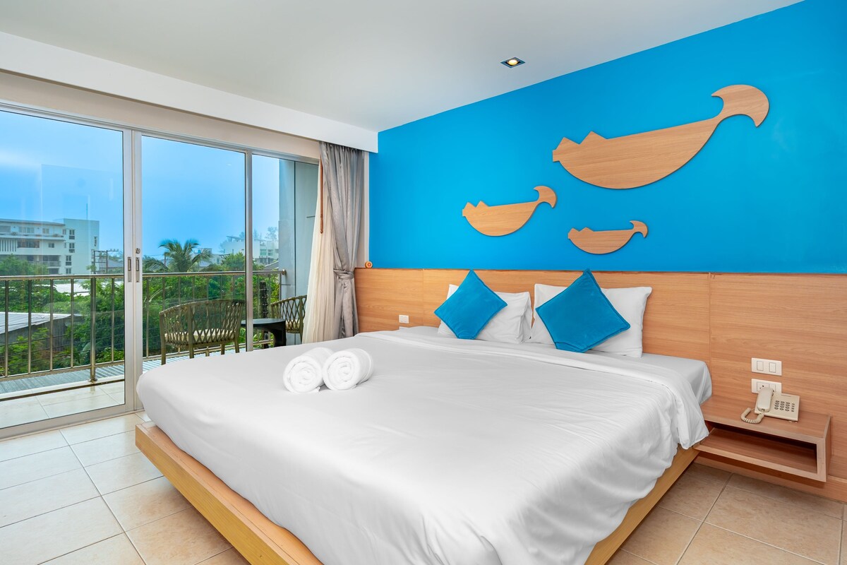 Une chambre d’hôtel avec un grand lit, un balcon offrant une belle vue et un mur bleu orné de motifs en bois découpés.