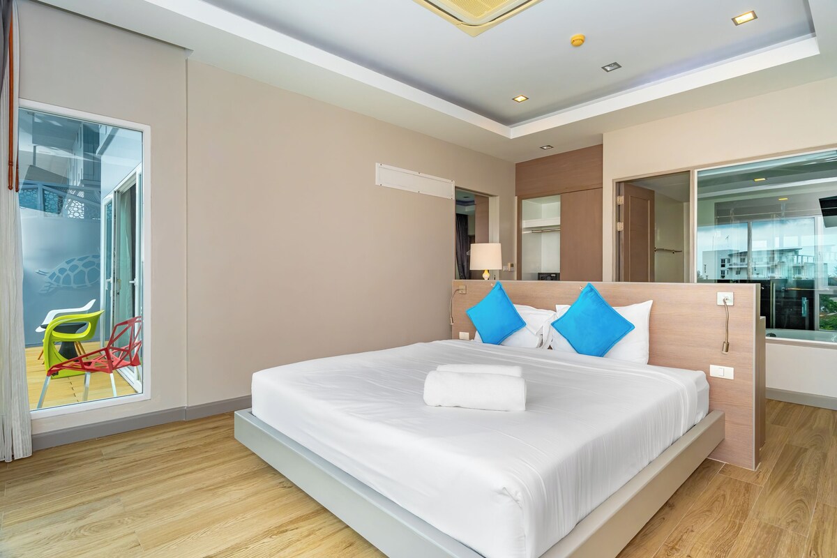A modern hotel room with a large bed, a sliding door to a balcony, and a view of the cityscape.