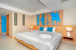A modern hotel room with a large bed, wooden headboard, two bedside lamps, and a wall art piece. - Ratana Platinum Resort Kamala (Kamala)