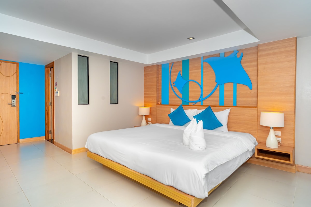 A modern hotel room with a large bed, two bedside lamps, a wooden headboard, and a blue abstract wall art piece.