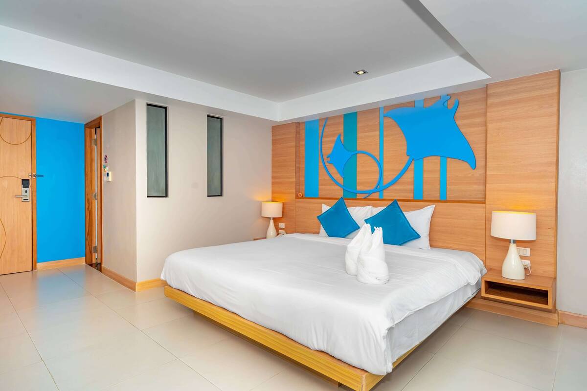 Een moderne hotelkamer met een groot bed, twee bedlampjes, een houten hoofdeinde en een blauw abstract kunstwerk aan de muur.