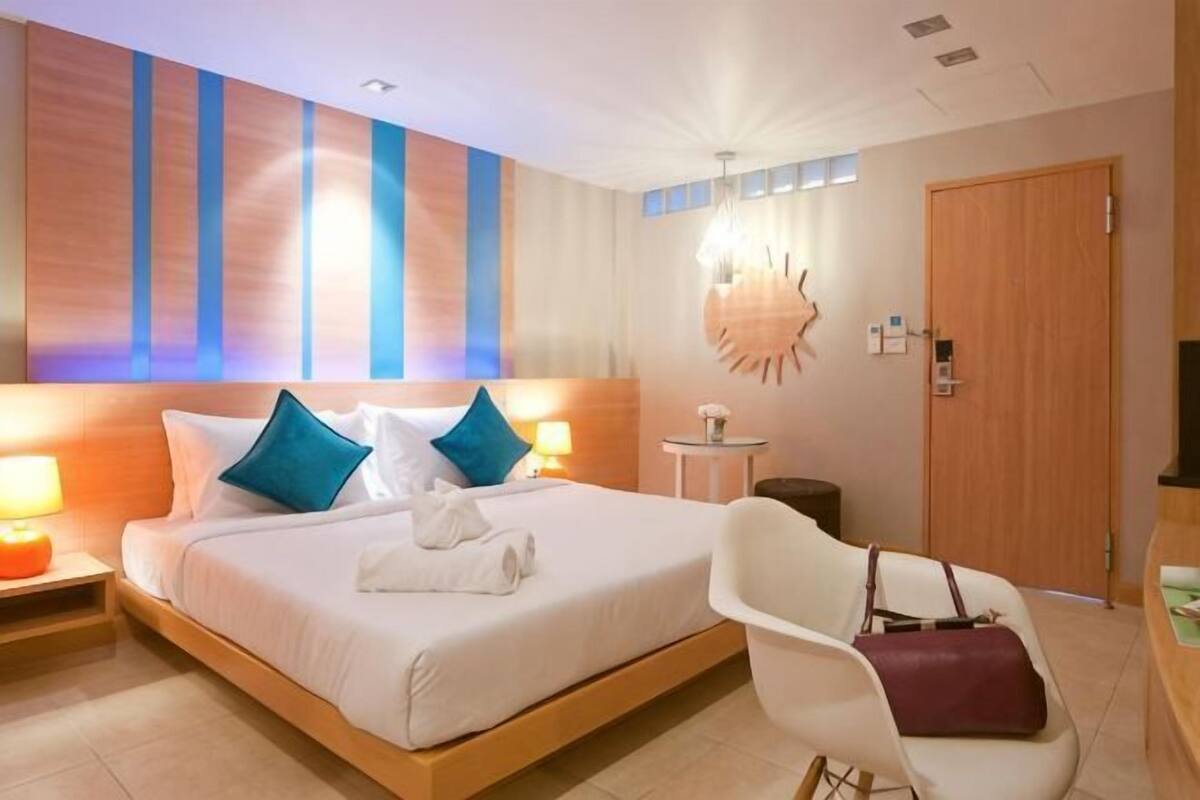 Een hotelkamer met een groot bed, bedlampjes, een stoel, een houten deur en een wandlamp.