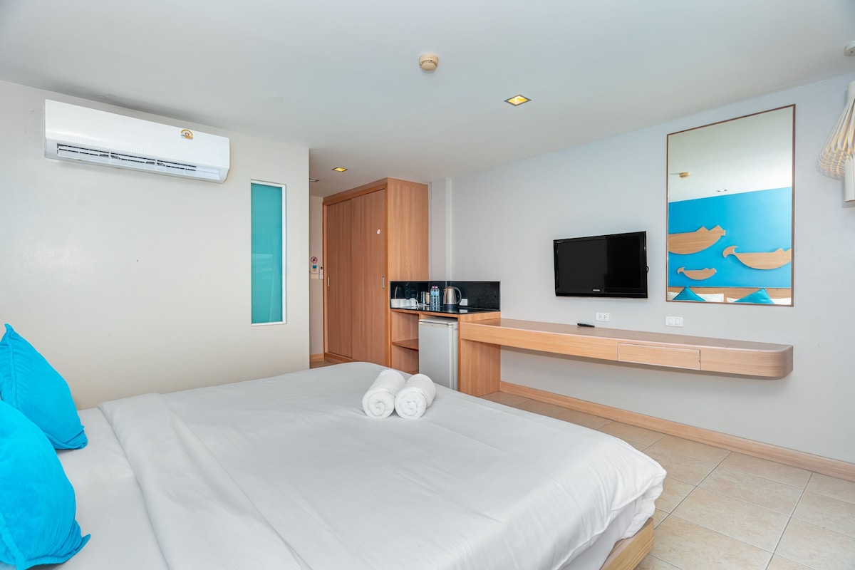A hotel room with a bed, a TV, a desk with a computer, and a kitchenette.