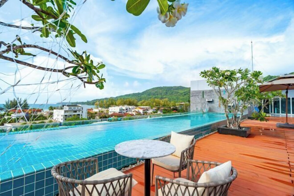 Une piscine sur le toit offrant une vue sur un paysage montagneux, une table ronde avec des chaises et une plante en pot.