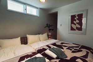 Un dormitorio con cama, almohadas, una mesita de noche con una planta y un cuadro en la pared.