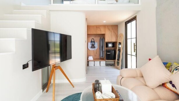A modern living room with a flat-screen TV, a sofa, a coffee table, and a kitchen area in the background. - Chunnchay Bed&Restaurant (Mae Wang)