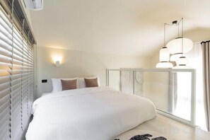 A bedroom with a large bed, a bedside table, a lamp, and a window with blinds. - Chunnchay Bed&Restaurant (Mae Wang)
