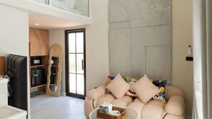 A modern living room with a sofa, a coffee table, and a built-in TV. There is a wooden cabinet and a door leading to another room. - Chunnchay Bed&Restaurant (Mae Wang)