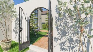 A gated entrance with a pathway leading to a building, surrounded by greenery and a clear sky. - Chunnchay Bed&Restaurant (Mae Wang)