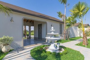 A house with a covered porch, a white fountain, and a well-maintained garden with palm trees. - Chunnchay Bed&Restaurant (Mae Wang)