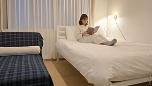 Een kamer met een bed, nachtkastje, lamp en een raam met gordijnen.