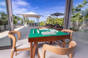 A dining area with a green table, wooden chairs, and a view of a pool and lounge chairs. - Sava Villa 6 Villa Roxo (Takua Thung)