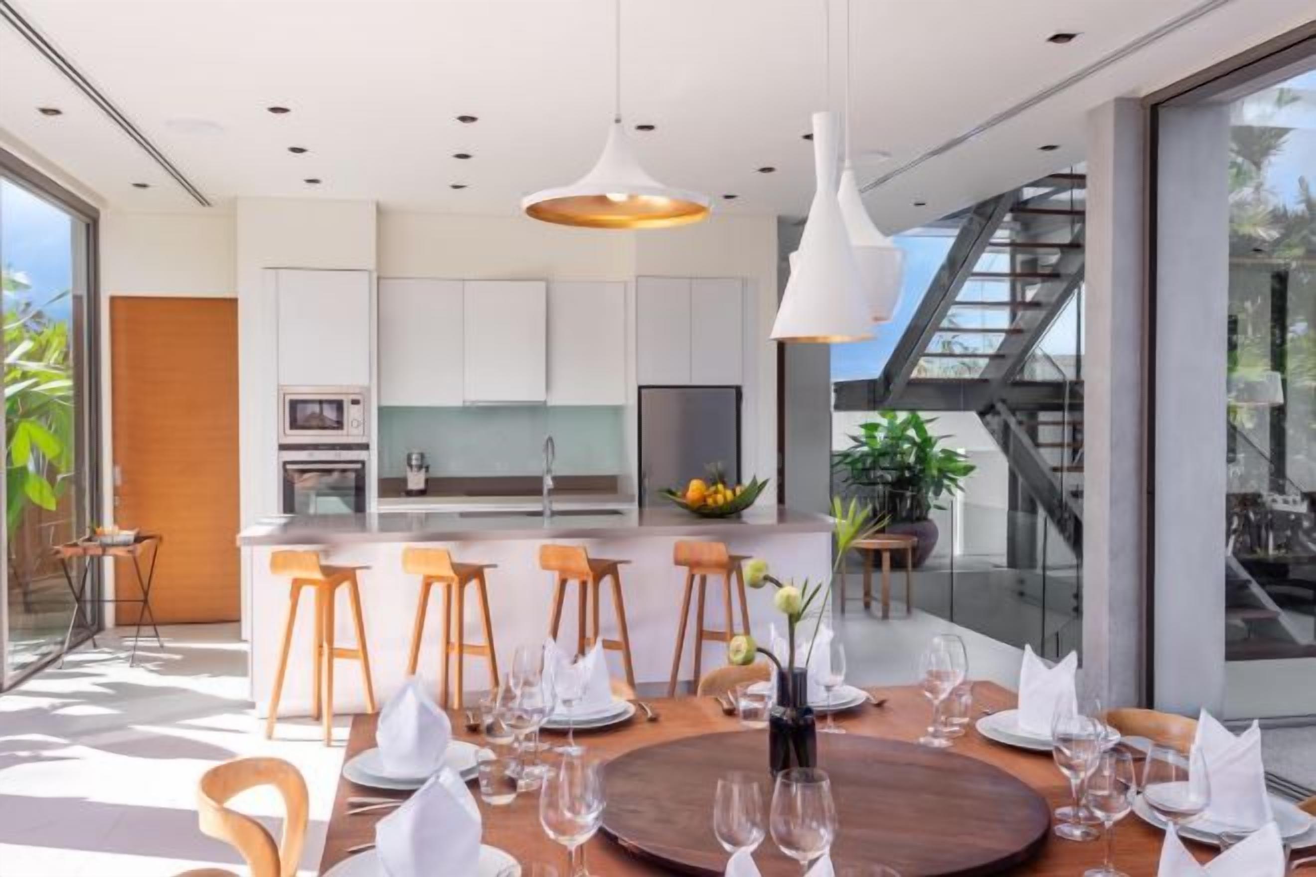 A modern kitchen with white cabinets, a central island, and a dining area with a round table and chairs.