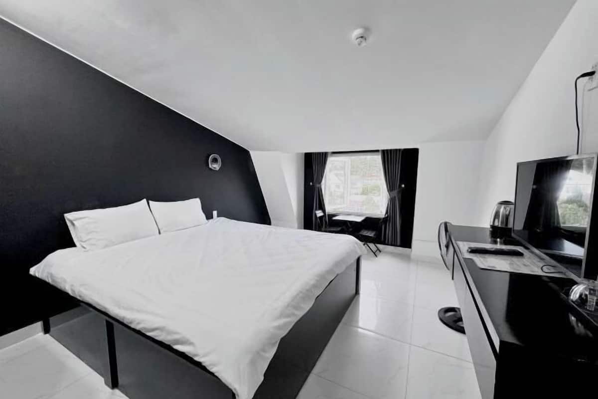 A modern hotel room with a bed, a desk, a television, and a window with curtains.