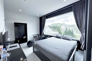 A modern hotel room with a large bed, a desk, a flat-screen TV, and a view of a cityscape.