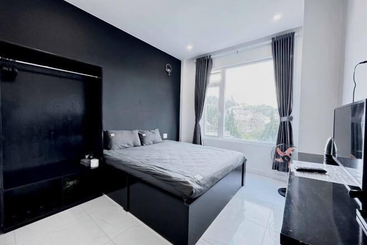 A modern bedroom with a bed, a desk with a computer, a TV, and a window with curtains.