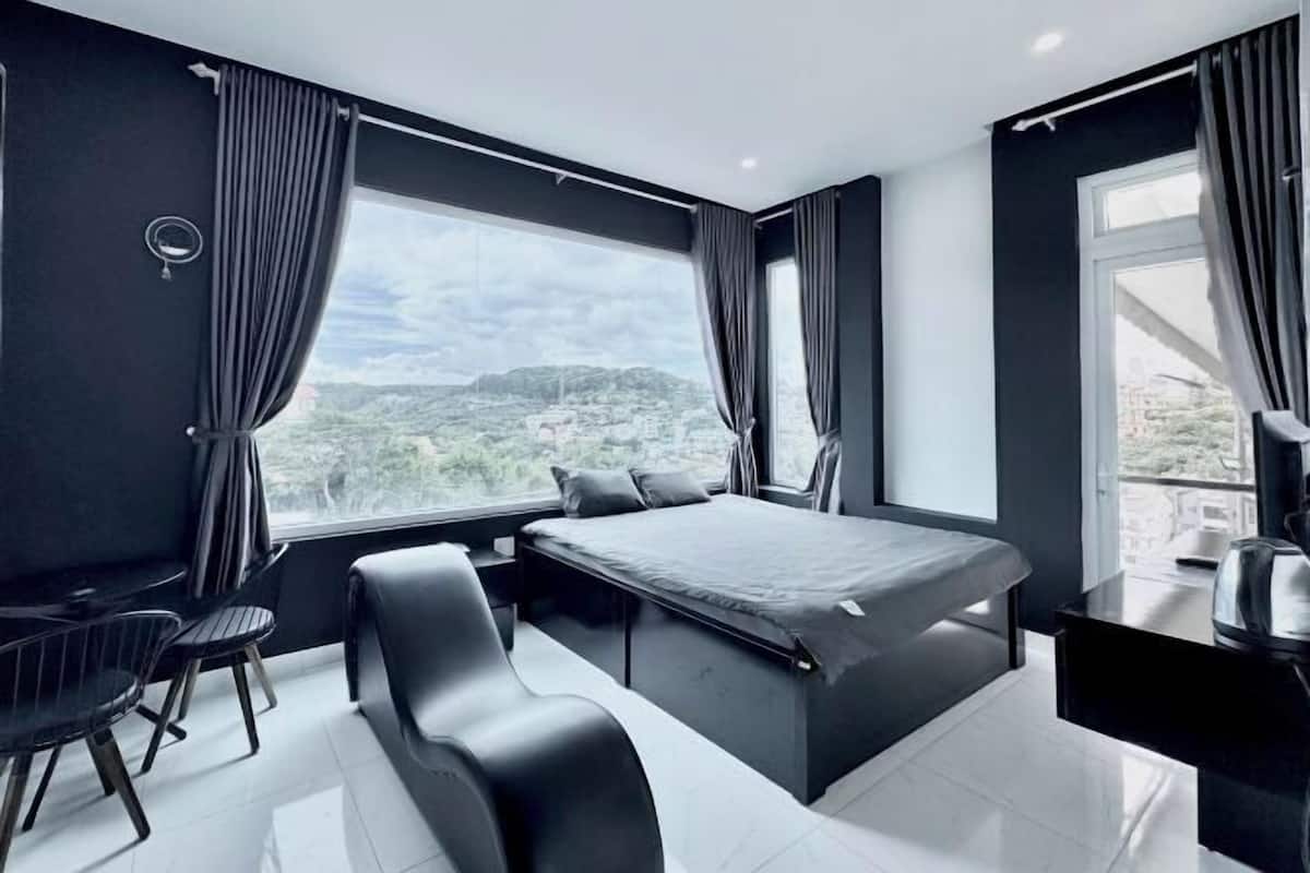 A modern bedroom with a bed, a desk, and a chair, featuring a large window with a city view.
