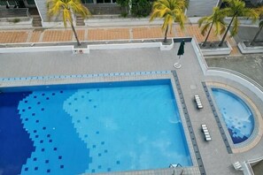 Une piscine sur le toit, avec une fontaine à eau d’un bleu limpide, entourée de palmiers et bordée d’une allée pavée.