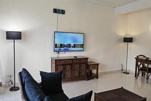 A living room with a flat-screen TV, two floor lamps, a sofa, a wooden cabinet, and a small table. - Langkawi Perdana Families Suite @ Langkawi Airport (Langkawi)