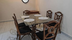 A dining area with a glass-top table, six wooden chairs with black cushions, and a small wooden side table. - Langkawi Perdana Families Suite @ Langkawi Airport (Langkawi)