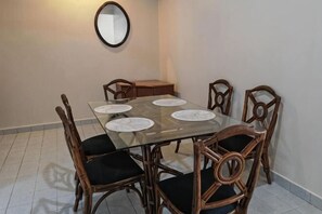 A dining area with a glass-top table, six wooden chairs with black cushions, and a small wooden side table. - Langkawi Perdana Families Suite @ Langkawi Airport (Langkawi)