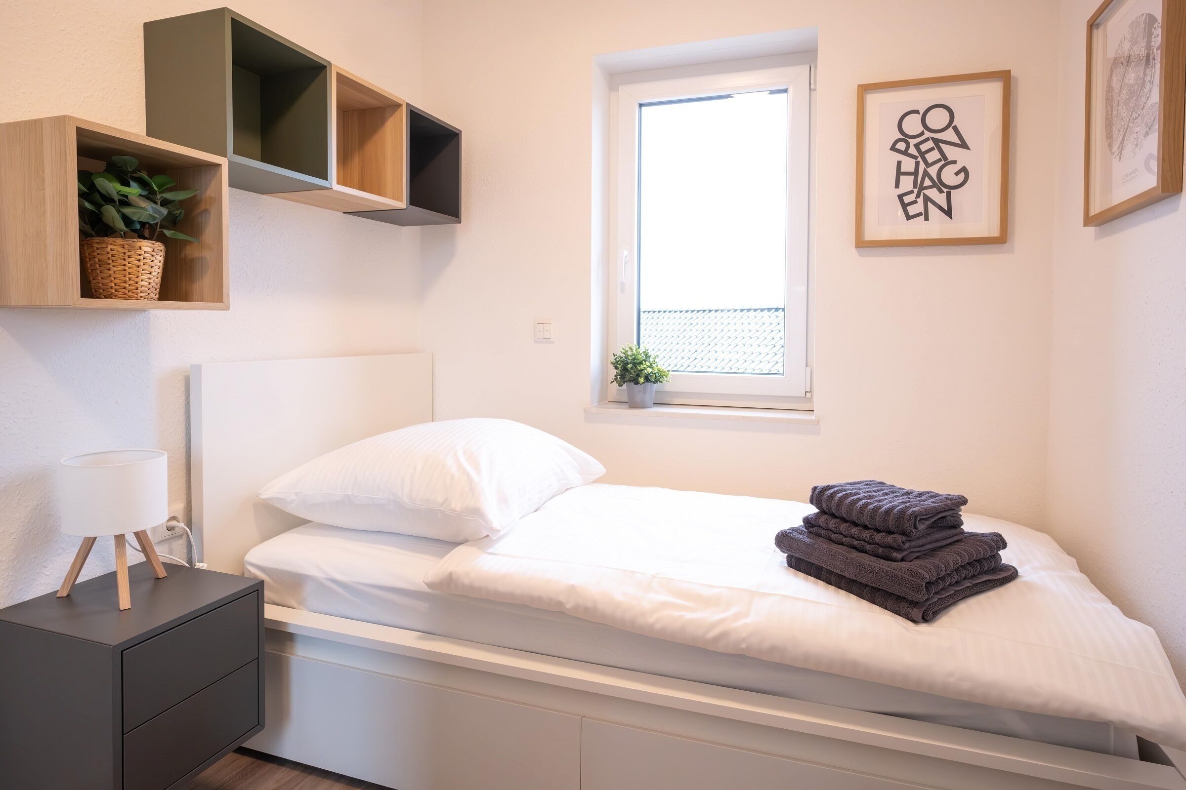 A bedroom with a bed, bedside table, lamp, and a window with a view.