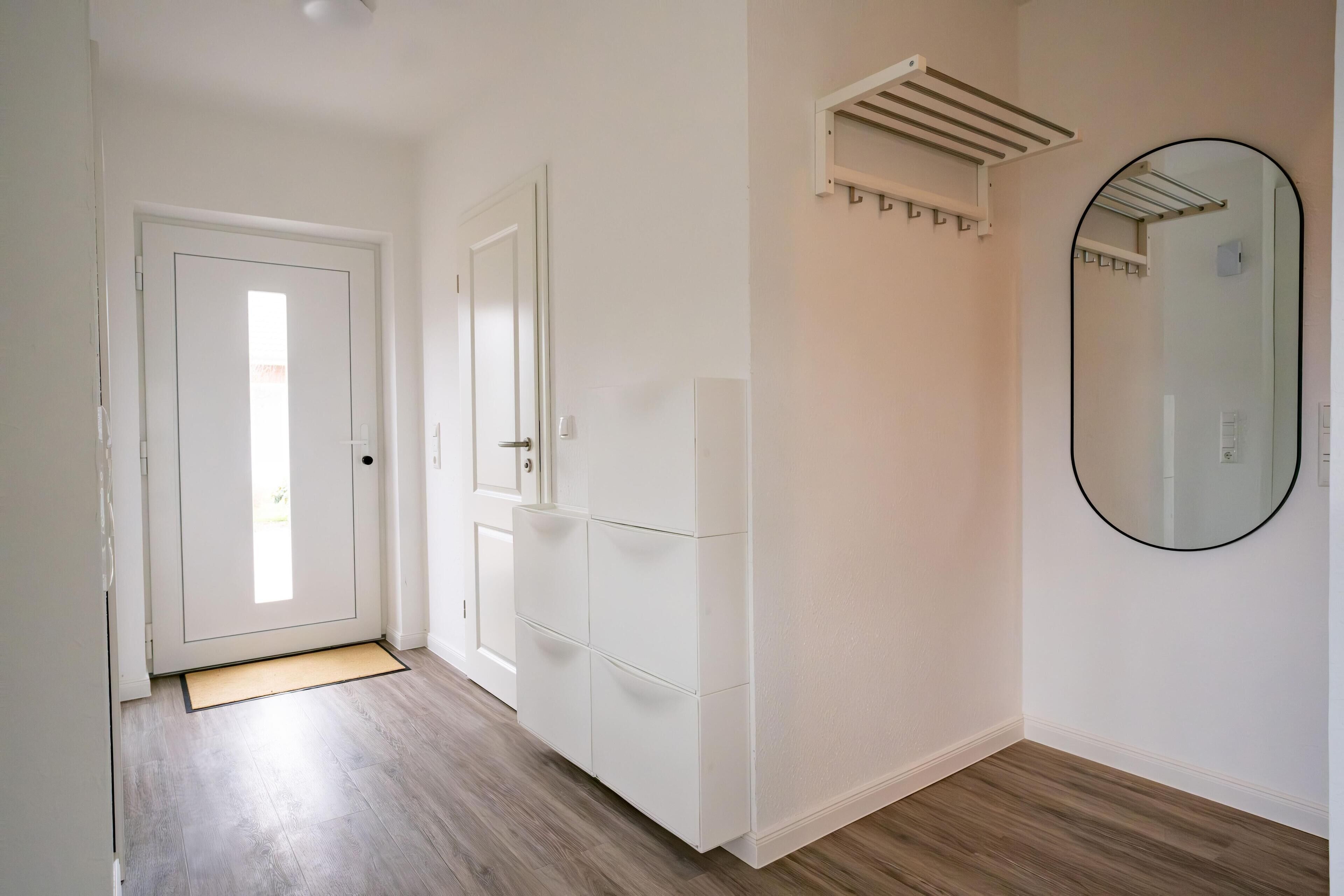 A hallway with a white door, a white cabinet with drawers, a towel rack, and a mirror on the wall.