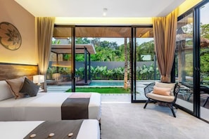 A hotel room with a bed, a chair, a table, and a view of a swimming pool and greenery.