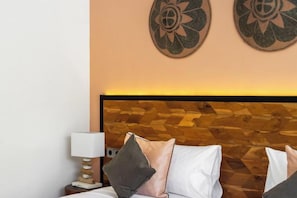 A hotel room with a wooden headboard, a bed with pillows, a nightstand with a lamp, and decorative wall art. - Villa Swing by BaliSuperHost (Bali)
