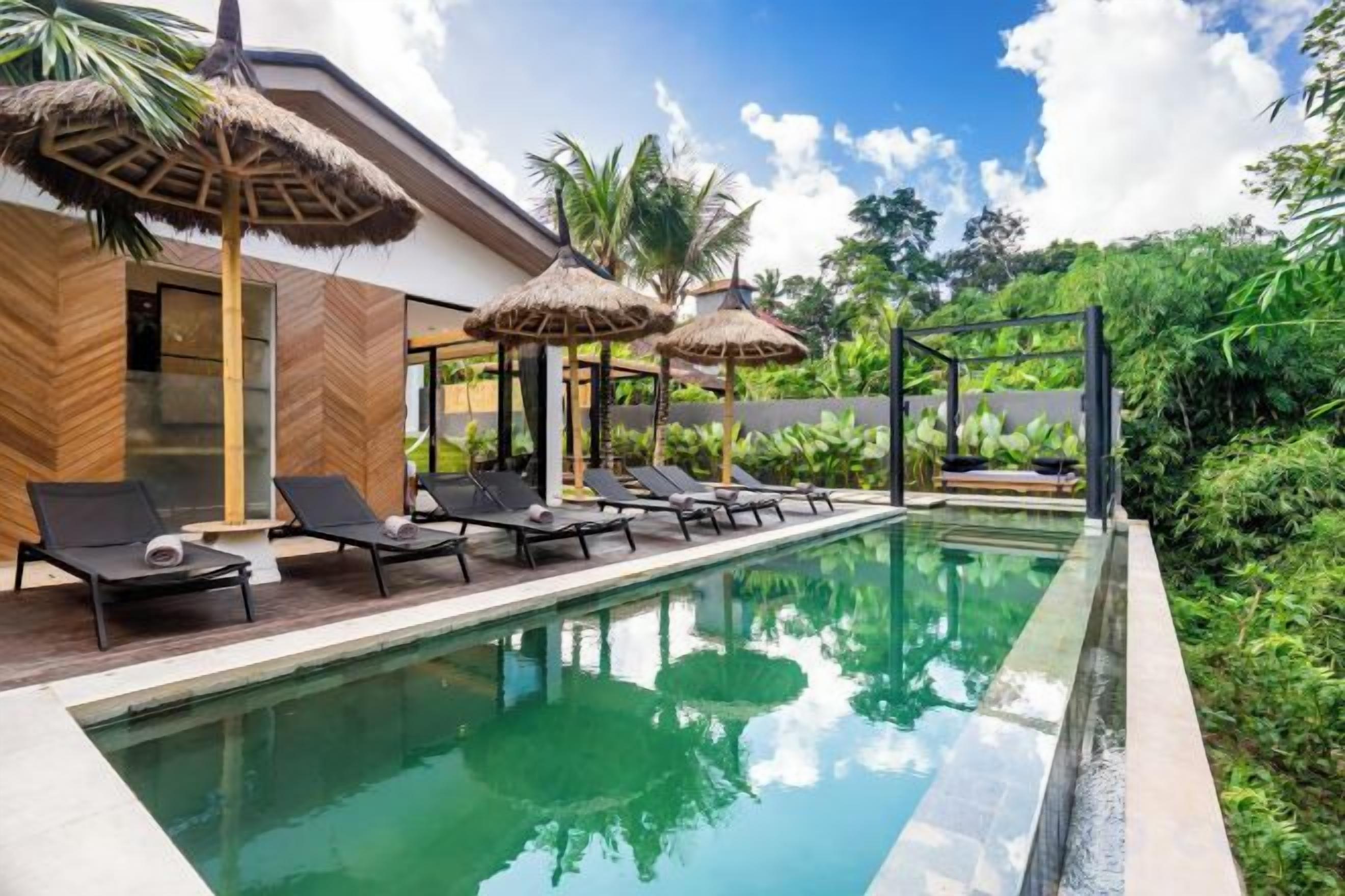 A pool area with lounge chairs and thatched umbrellas, surrounded by lush greenery.
