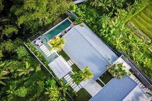 An aerial view of a resort with a swimming pool, lounge chairs, and a covered area.