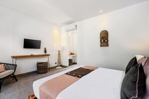 A modern hotel room with a bed, a desk, a television, and a wall-mounted TV.