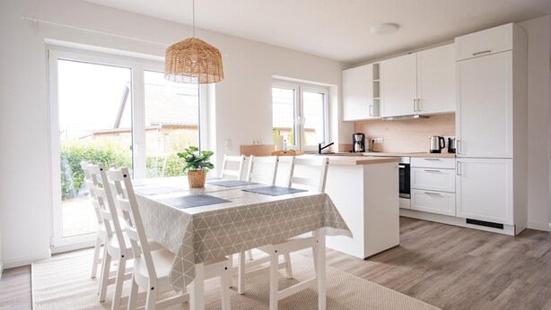 A modern kitchen with white cabinets, a central island, and a dining area with white chairs and a table.