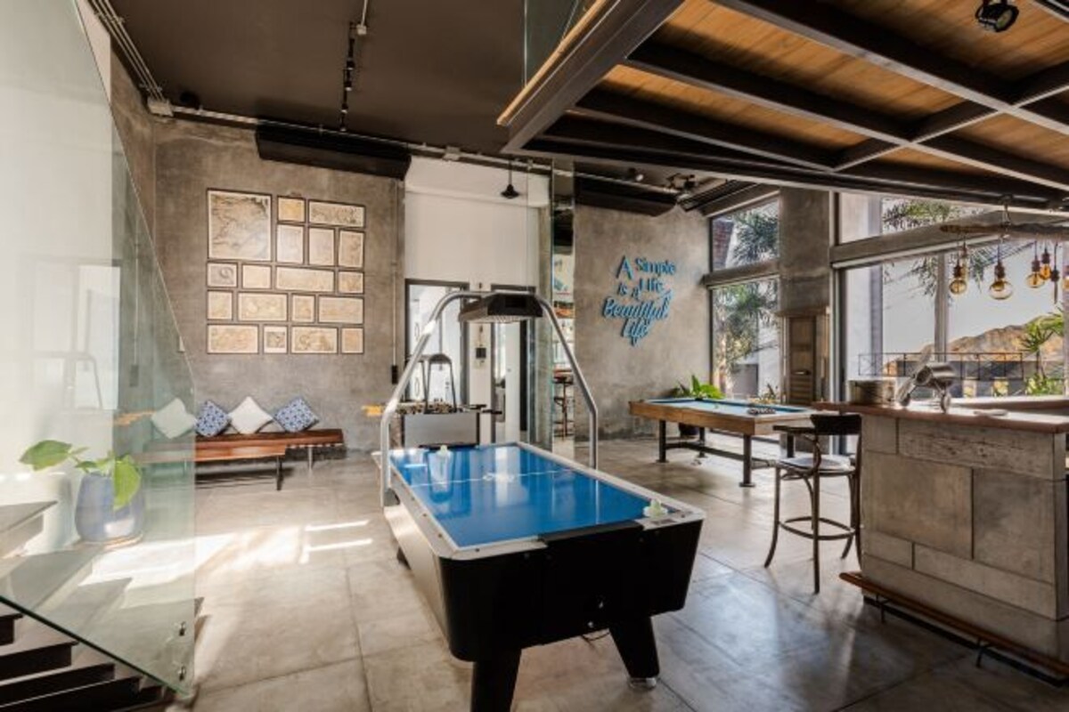 Una mesa de billar en una sala con zona de bar, asientos y vistas al exterior.