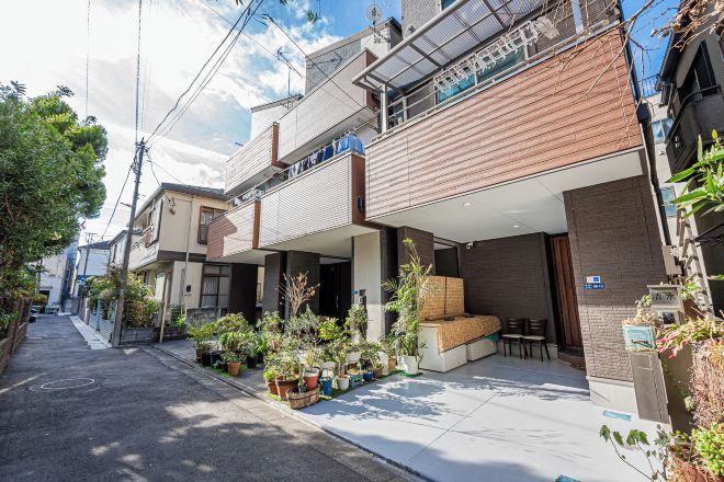 A narrow urban street with residential buildings, outdoor seating areas, and potted plants.