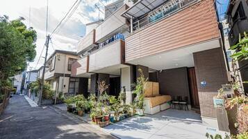 A narrow urban street with residential buildings, outdoor seating areas, and potted plants.