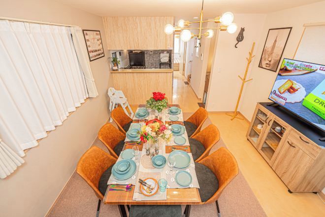 A dining area with a table set for six, a kitchen in the background, and a television on a cabinet.