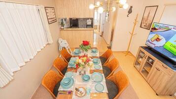 A dining area with a table set for six, a kitchen in the background, and a television on a cabinet.