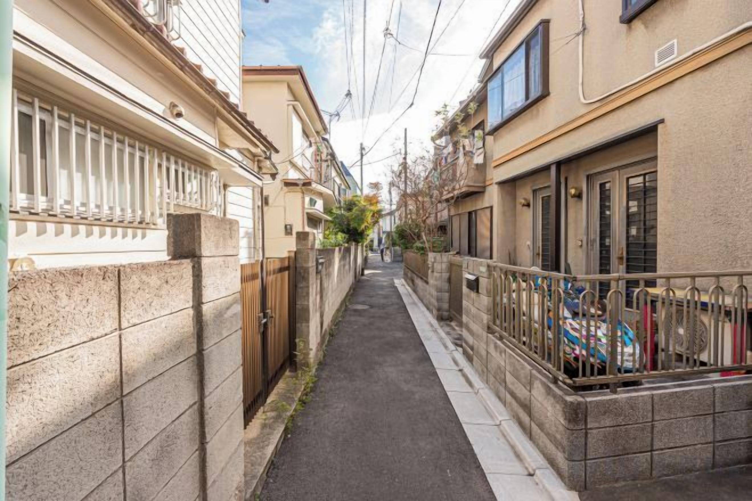 A narrow urban street with buildings on either side, a sidewalk, and a metal fence.